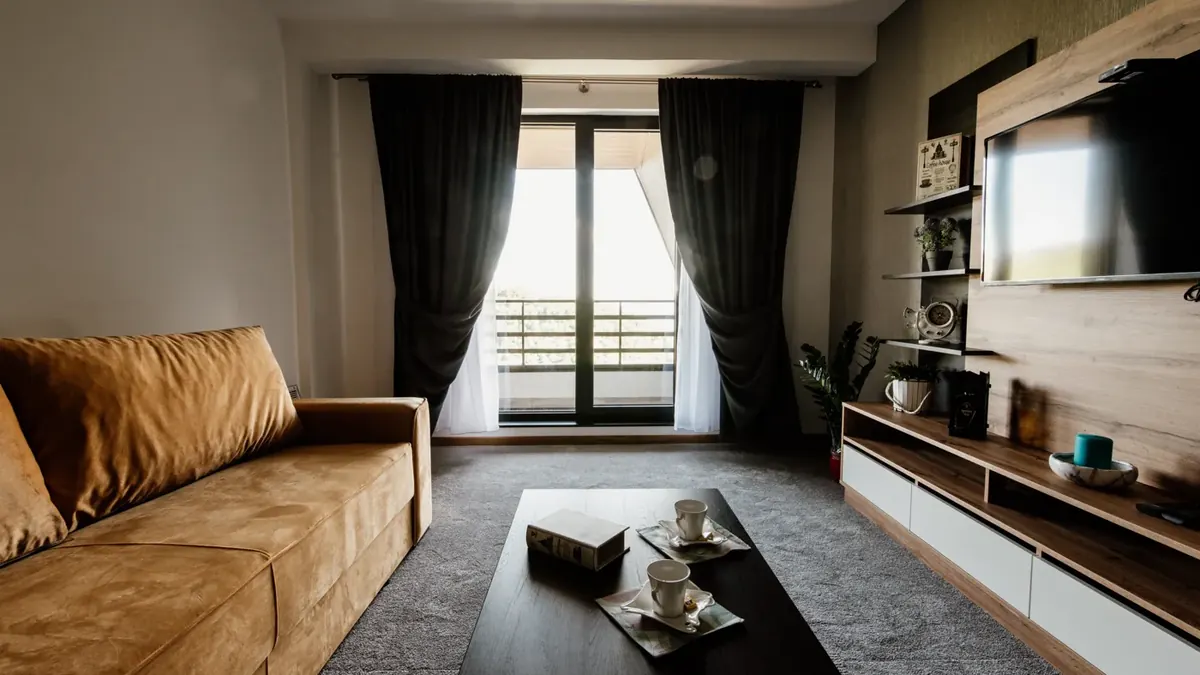 Sala com sofá marrom, mesa de madeira e grandes janelas