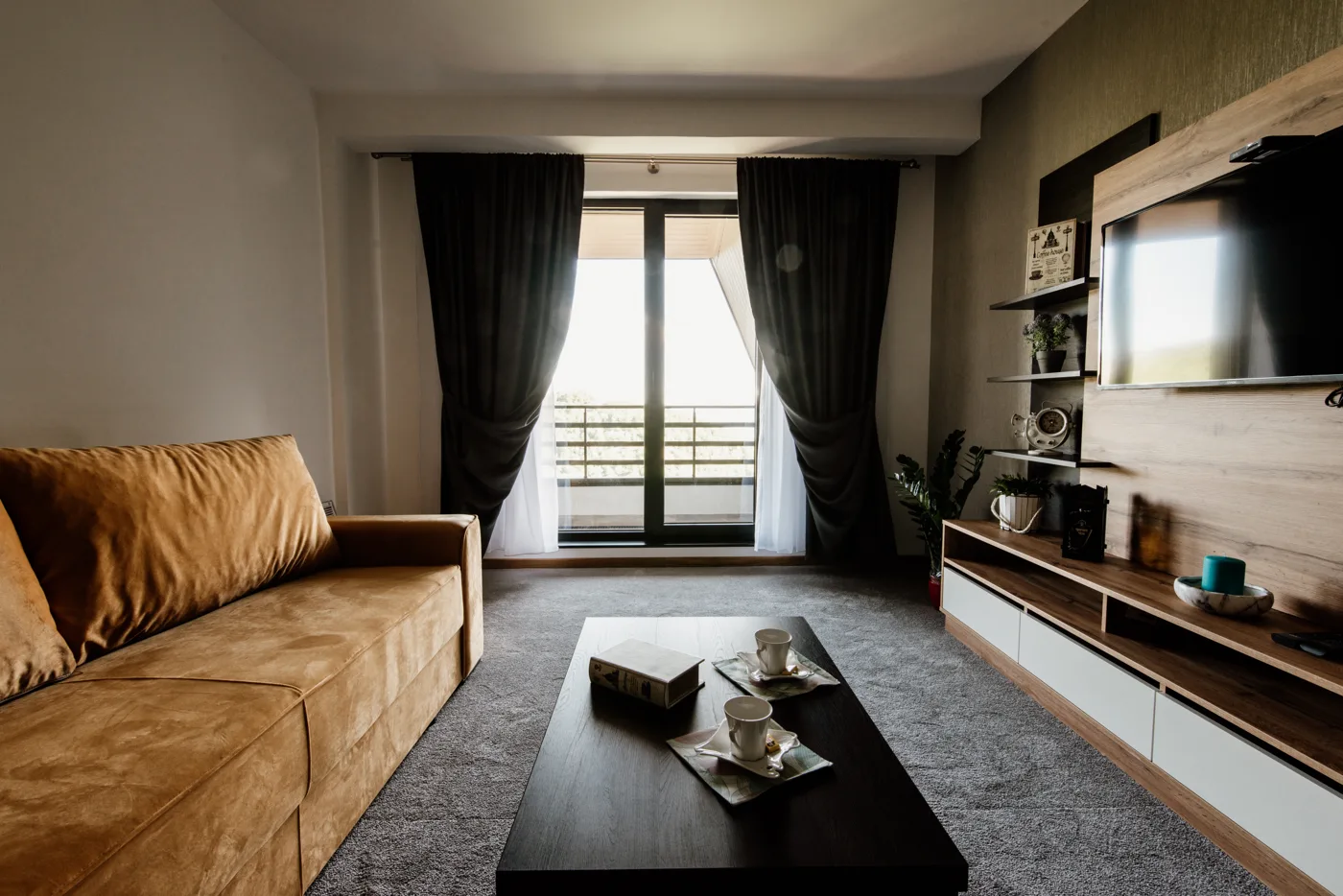 Sala com sofá marrom, mesa de madeira e grandes janelas